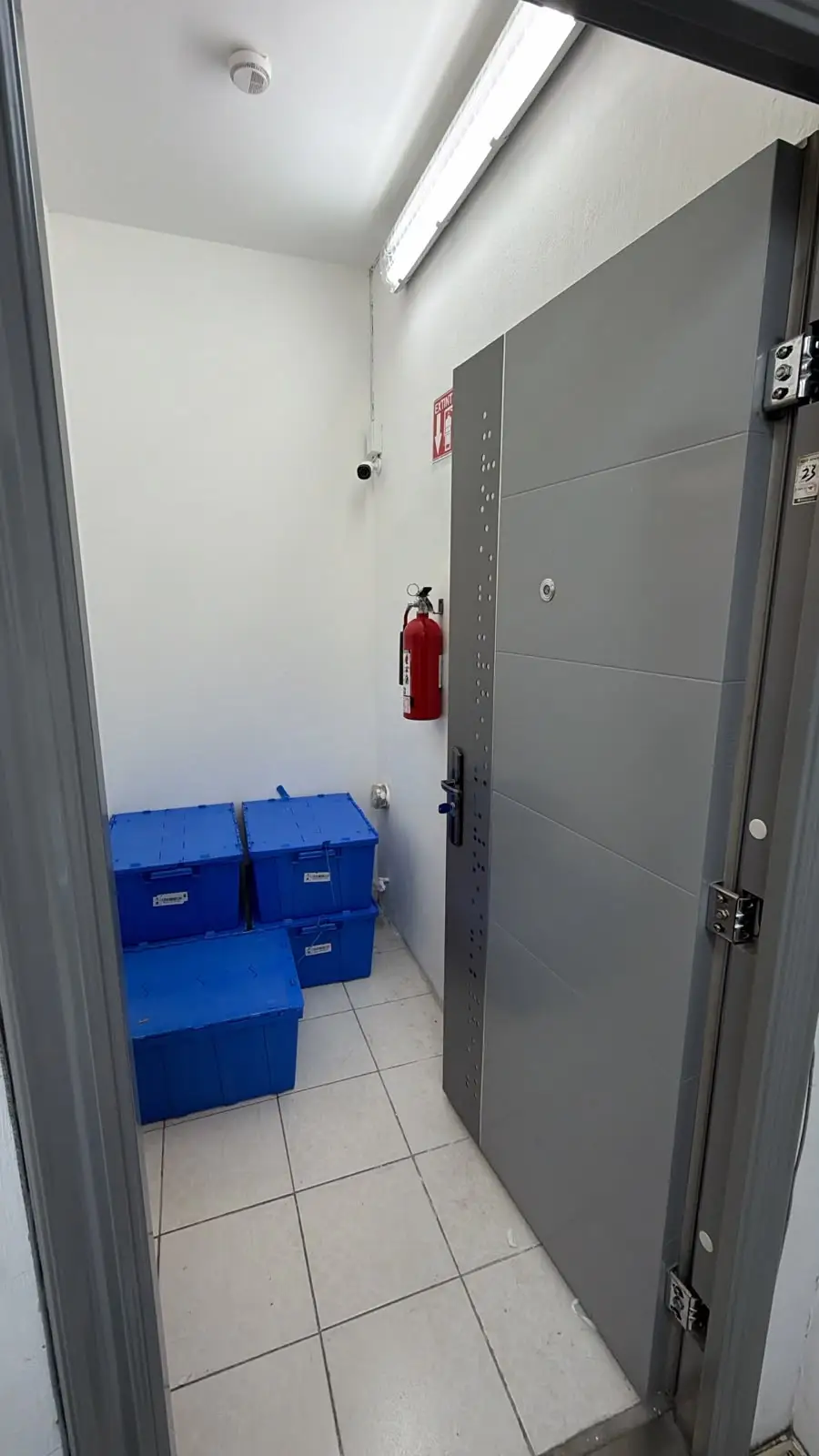 Puerta blindada abierta: al interior, cámara de vigilancia, detector de humo, extintor y contenedores sellados